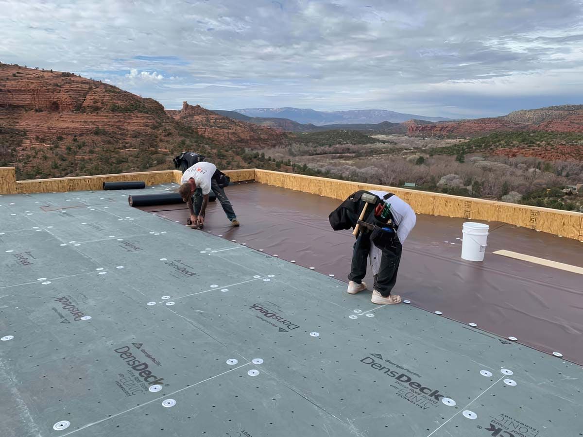Two workers installing roofing material on a flat roof with a scenic mountain backdrop.