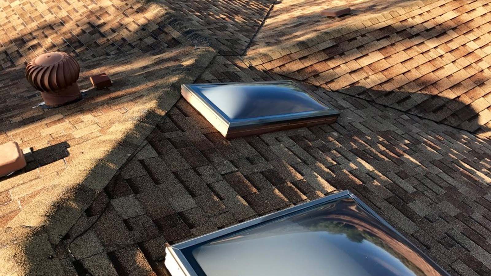 Close-up of a brown shingled roof with two skylights and a small vent.