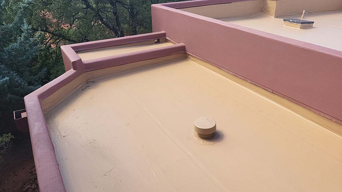 A low-slope roof coated in tan sealant, with pink edging. A small drain pipe is visible.