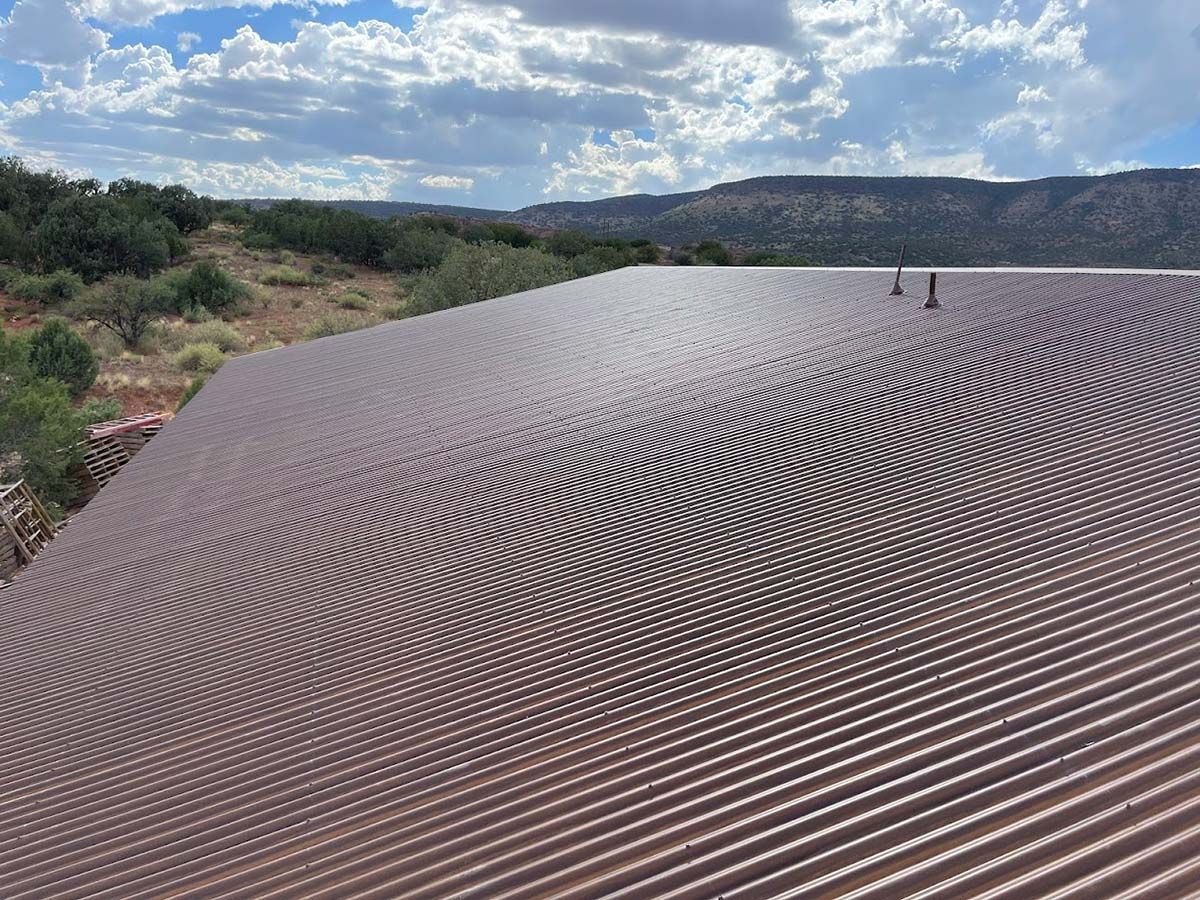 Brown corrugated metal roof on a building, with rolling hills and cloudy sky in the background.