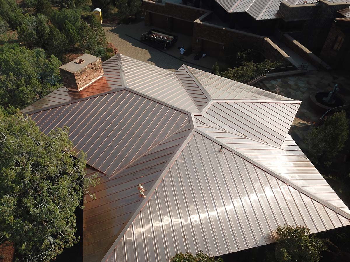 An aerial view of a house with a complex, shiny, metal roof.  A brick chimney is visible.