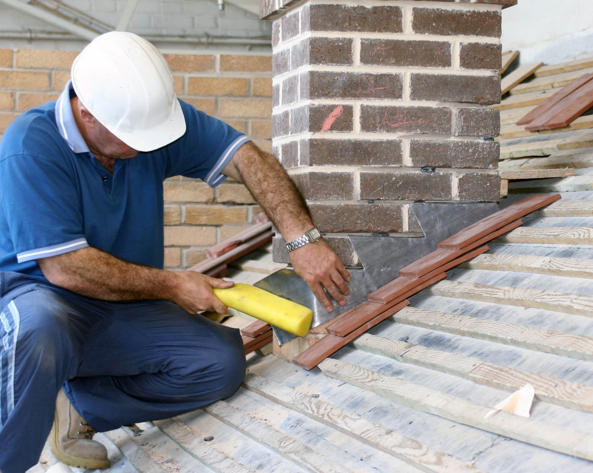 Roofer in white helmet installing flashing around a brick chimney on a tiled roof.