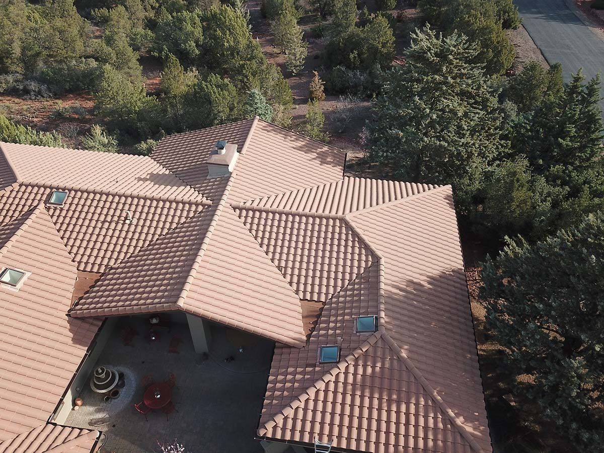 Overhead view of a terracotta-tiled roof with multiple peaks surrounded by green trees.