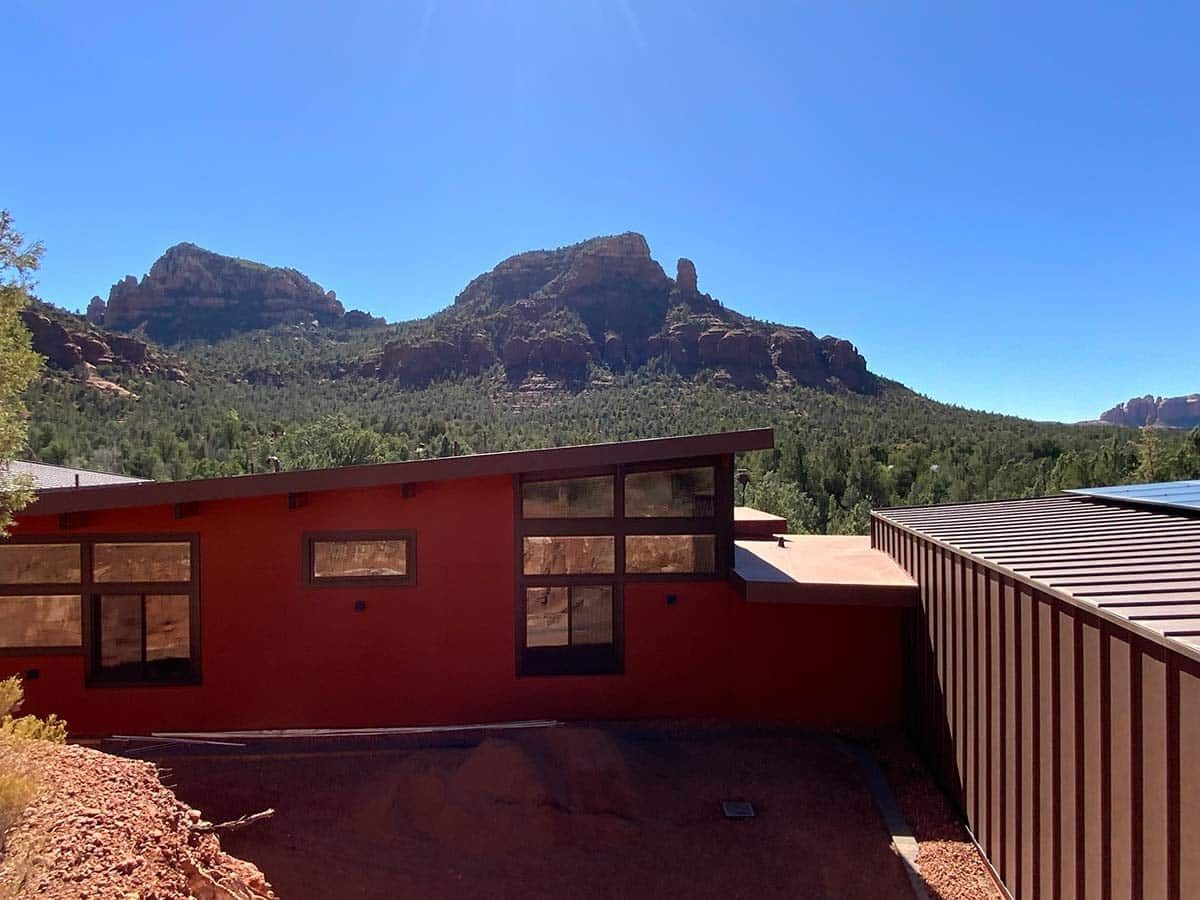 Red building with windows and angled roof against a backdrop of red rock mountains and a blue sky.