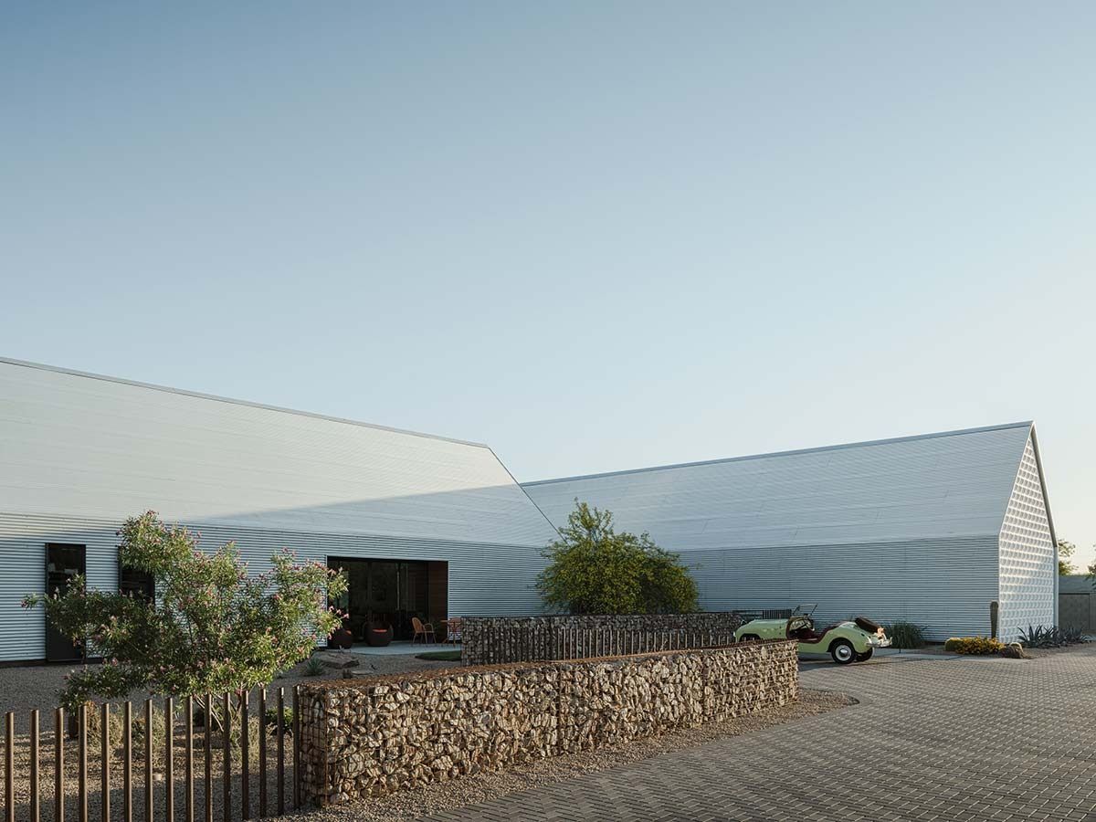 Modern white building with angled roof, stone wall, and small trees on a sunny day.
