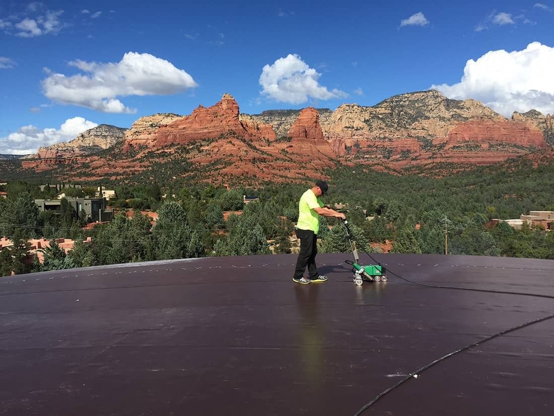 Person power washing a dark-colored roof with red rock mountains and blue sky in the background.