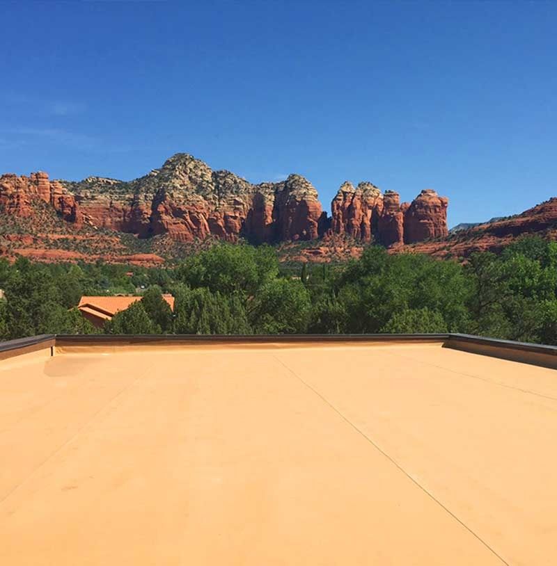 View of red rock formations, green trees, and blue sky from a flat, tan rooftop.