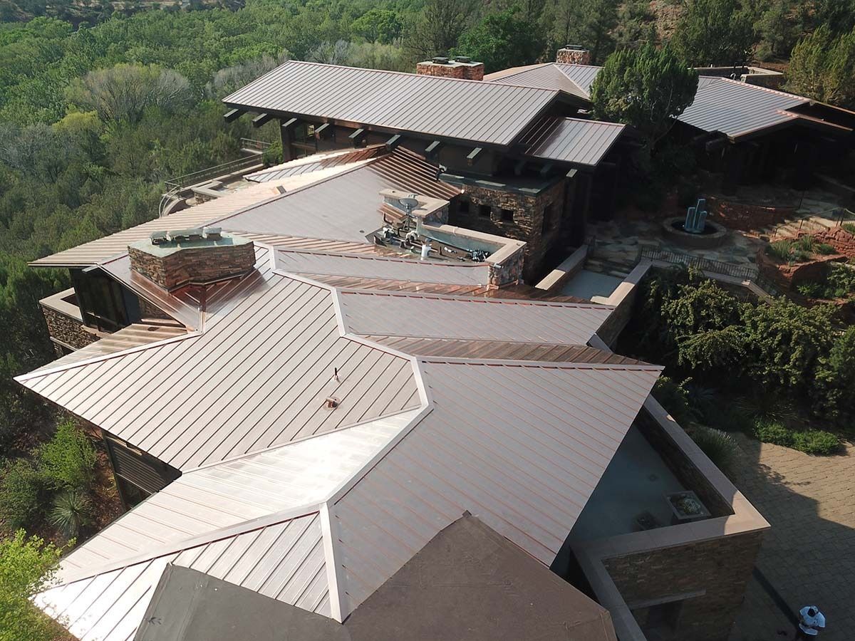 An aerial view of a multi-tiered copper-roofed house in a natural landscape.