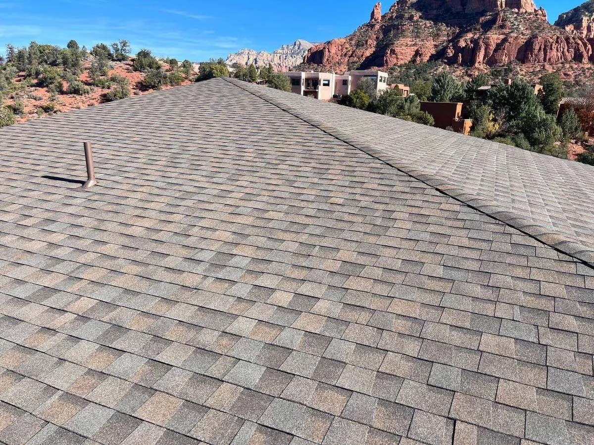 Asphalt shingle roof with mountain backdrop under a blue sky.