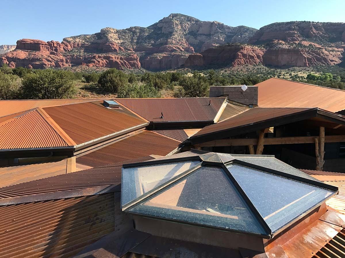 Roofs of various copper-toned textures with a skylight, set against a red rock mountain background.