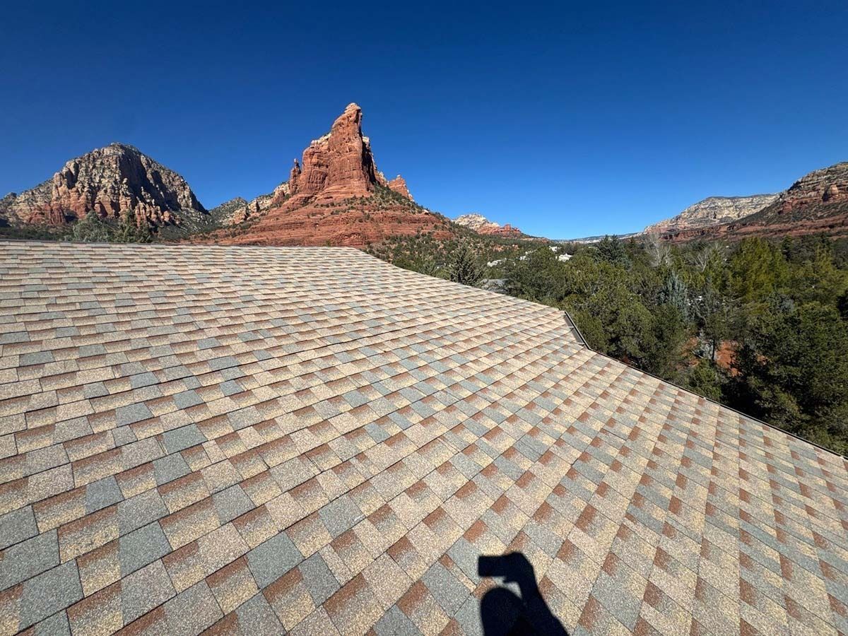 Rooftop with brown and gray shingles; scenic red rock mountain backdrop under a clear blue sky.