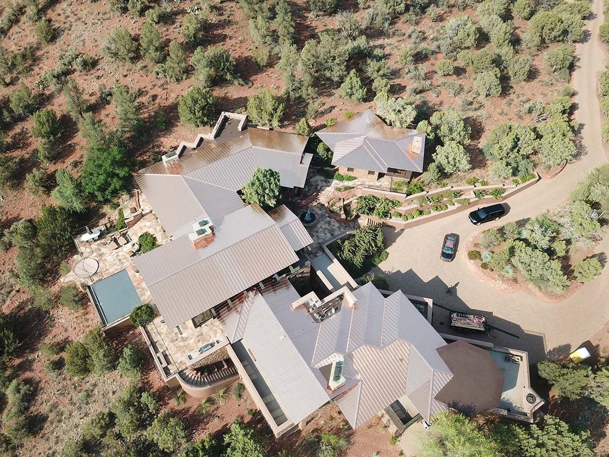 Aerial view of a multi-building home with a pool and vehicles in a natural, tree-covered landscape.