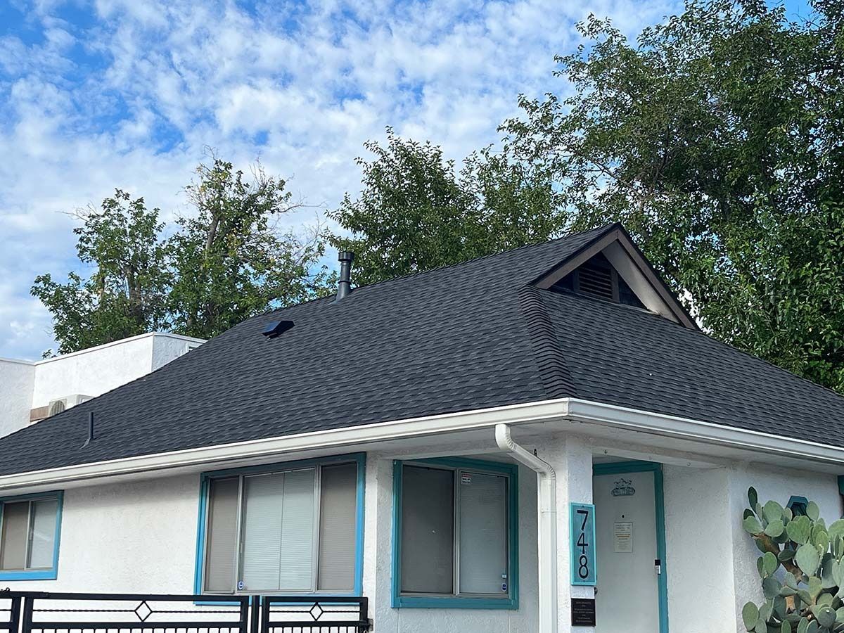 White building with blue trim, dark gray roof, and trees against a cloudy sky.