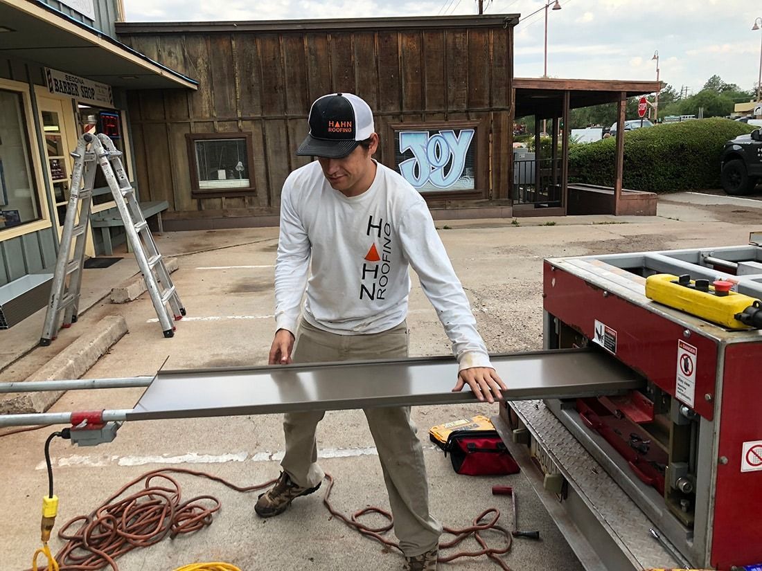 Man in a long-sleeve shirt operates machinery outdoors, holding a large, gray panel.