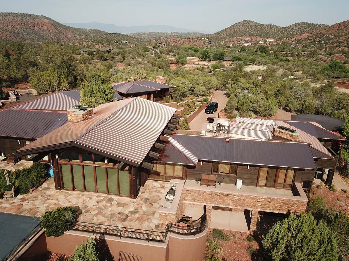 Aerial view of a brown, multi-sectioned house with a copper-colored roof in a hilly, desert landscape.