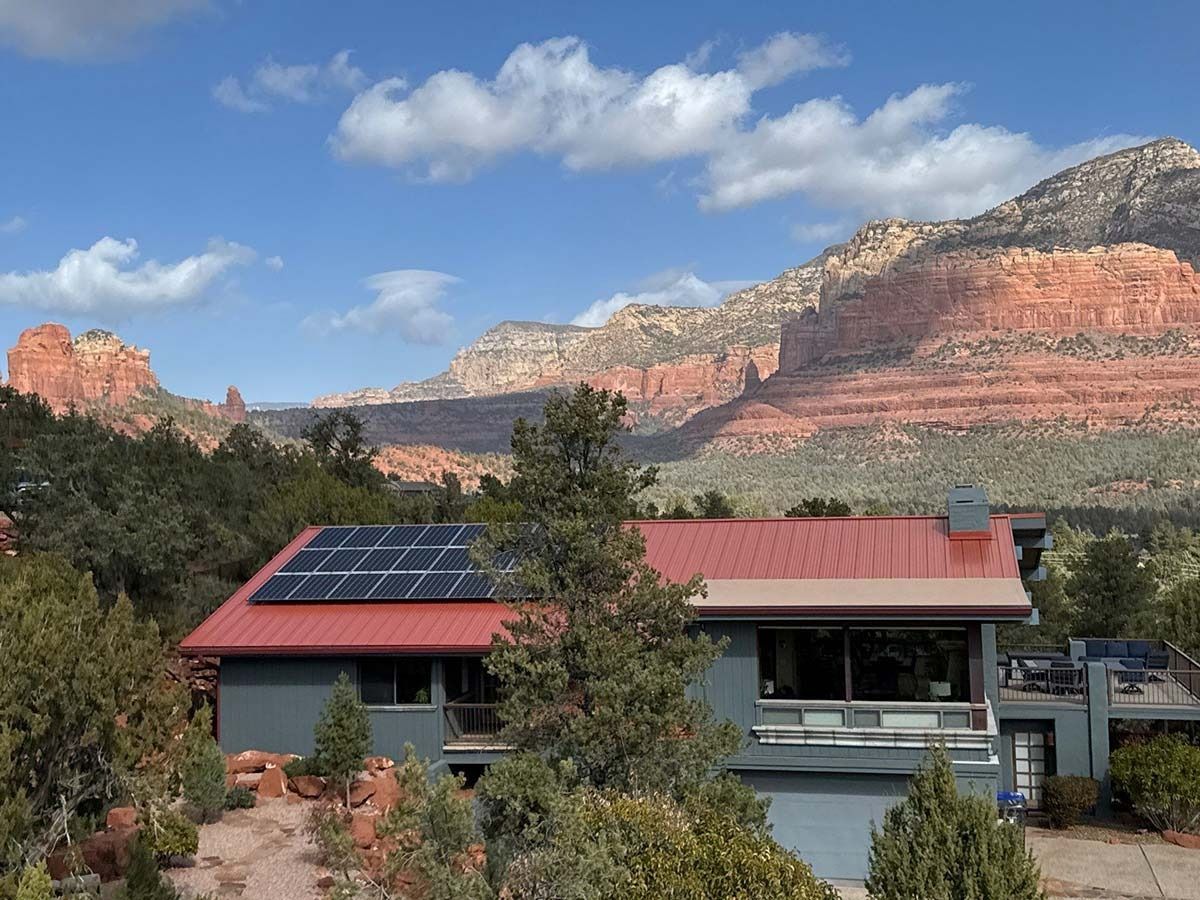 House with solar panels on a red roof, against a backdrop of red rock mountains and a blue sky.