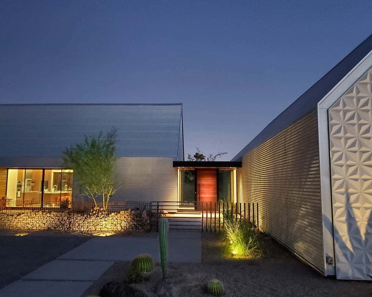 Modern house exterior with illuminated walls, red front door, and desert landscaping.