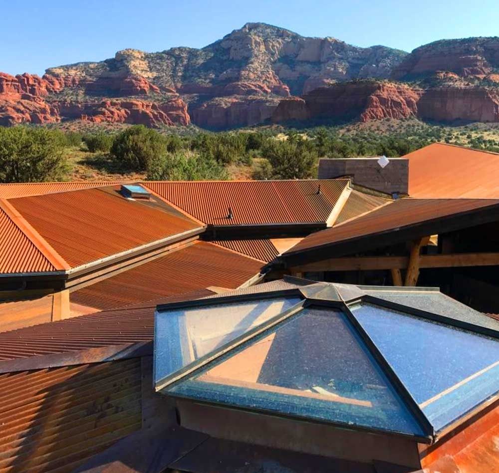 Rusty metal roof with skylights, against a backdrop of red rock mountains.