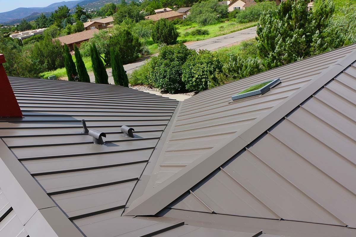 Metal roof with angled panels, brown color, with a view of houses and trees in background.