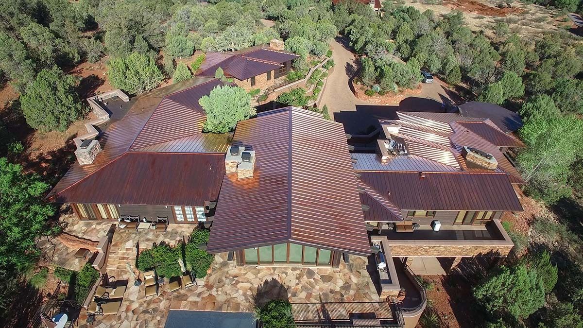 Aerial view of a unique, multi-sectioned house with a patterned copper roof, surrounded by trees.