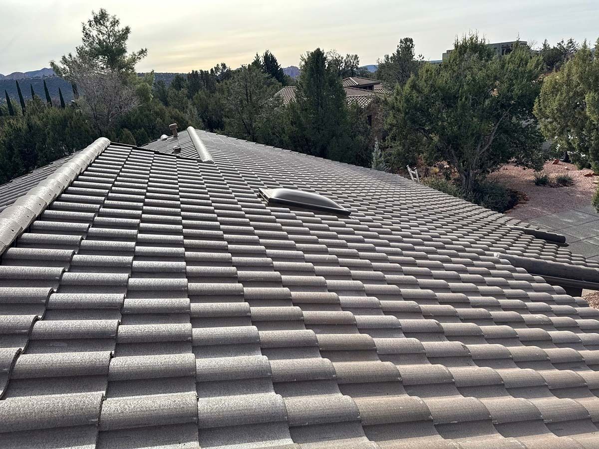View of a tile roof with damaged sections. Trees and sky are in the background.