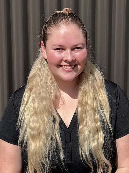 Woman with blonde hair smiles at the camera, wearing a black shirt in front of a neutral background.