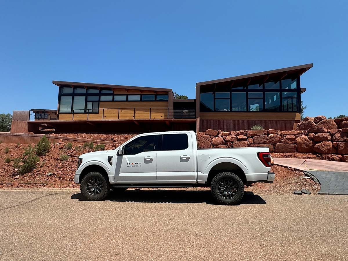 White pickup truck parked in front of a modern home with large windows on a sunny day.
