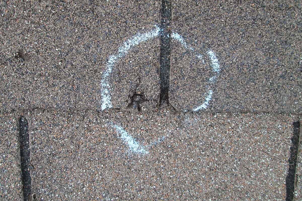 Close-up of asphalt shingle roof. A circled area with white paint around a hole.