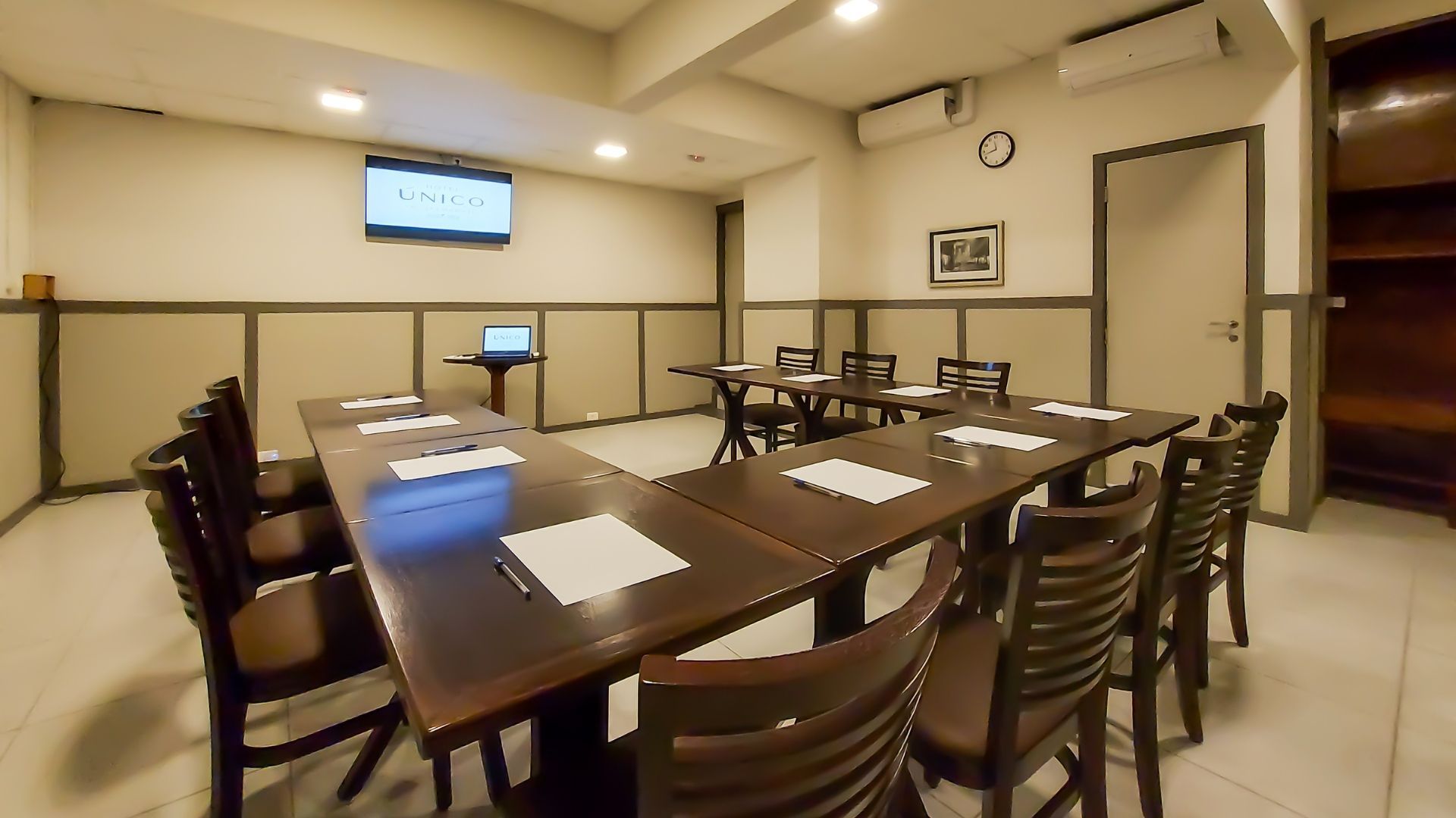 Uma sala de conferências com mesas e cadeiras e uma televisão na parede.