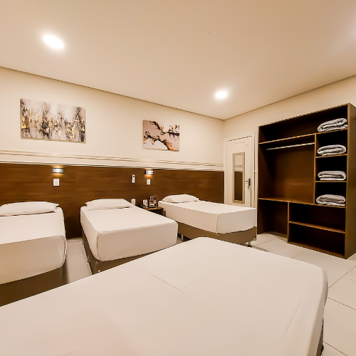 Um quarto de hotel com três camas e um armário.