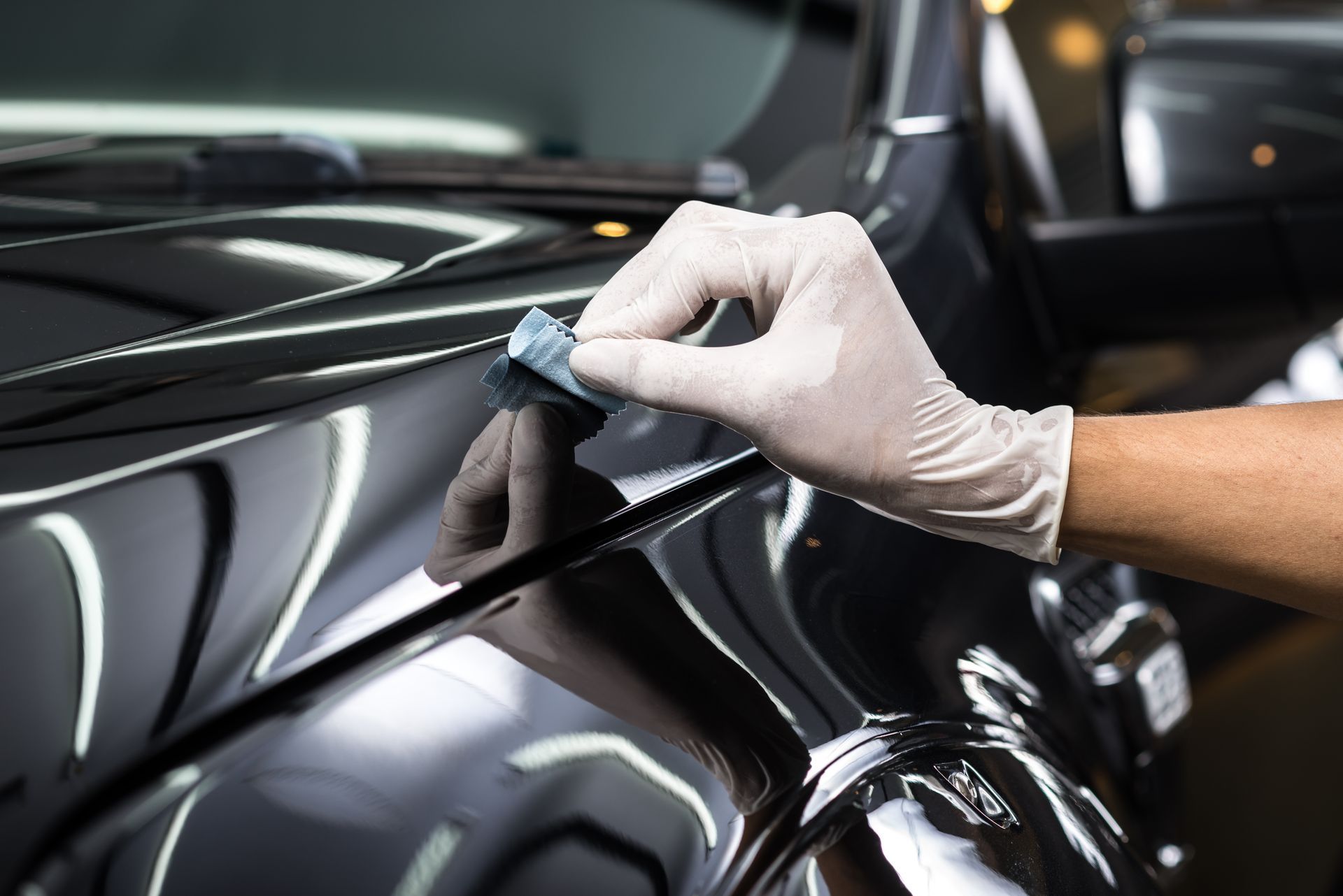 Gloved hand applying ceramic coating to a shiny black car surface.