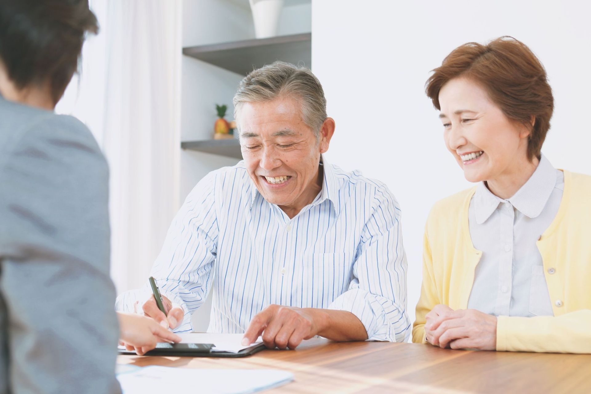 An elderly couple is sitting at a table signing a document.