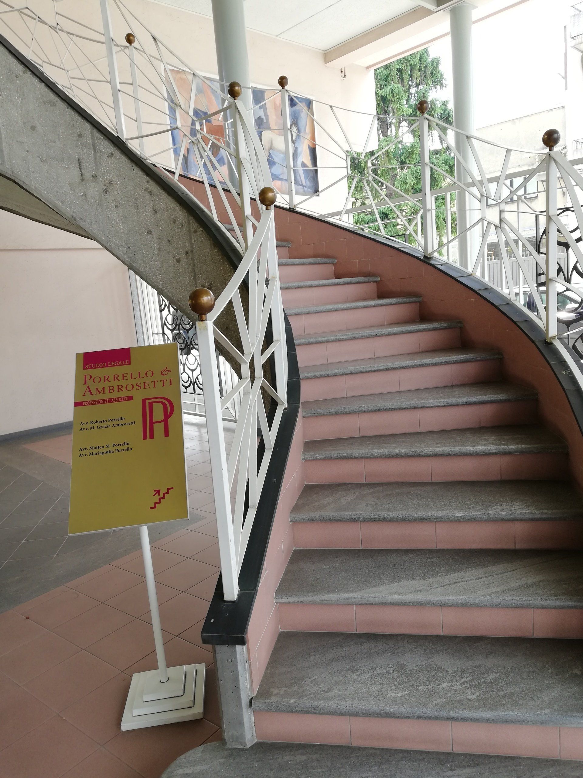 Scala a chiocciola con gradini rosa, ringhiera bianca e cartello giallo.