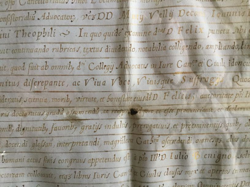 Primo piano di un documento con testo scritto a mano con inchiostro sbiadito, con alcune macchie e un buco nero.