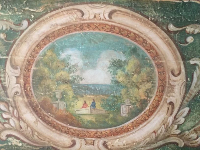 Dipinto ovale raffigurante un paesaggio con due figure sedute. Bordo verde con dettagli ornati bianchi e dorati.