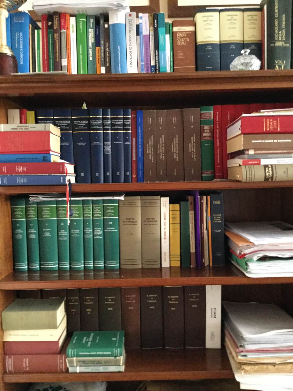 Libreria in legno piena di libri di vario tipo, per lo più con copertina rigida e di diversi colori, in un ambiente domestico.