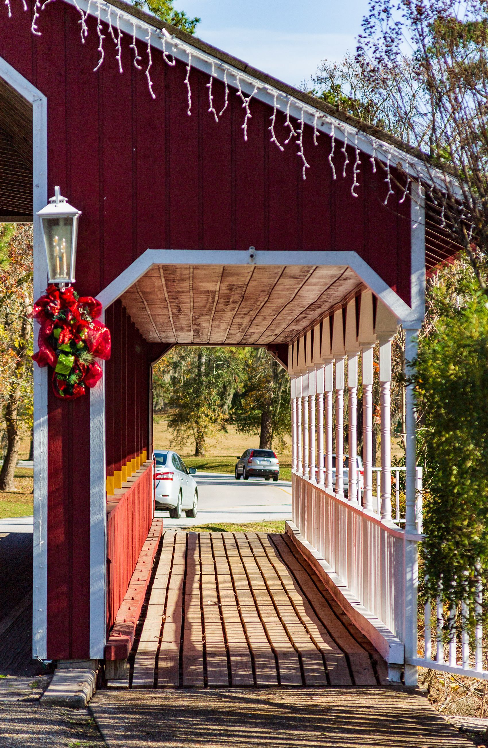 A red and white covered bridge with christmas lights hanging from the roof.