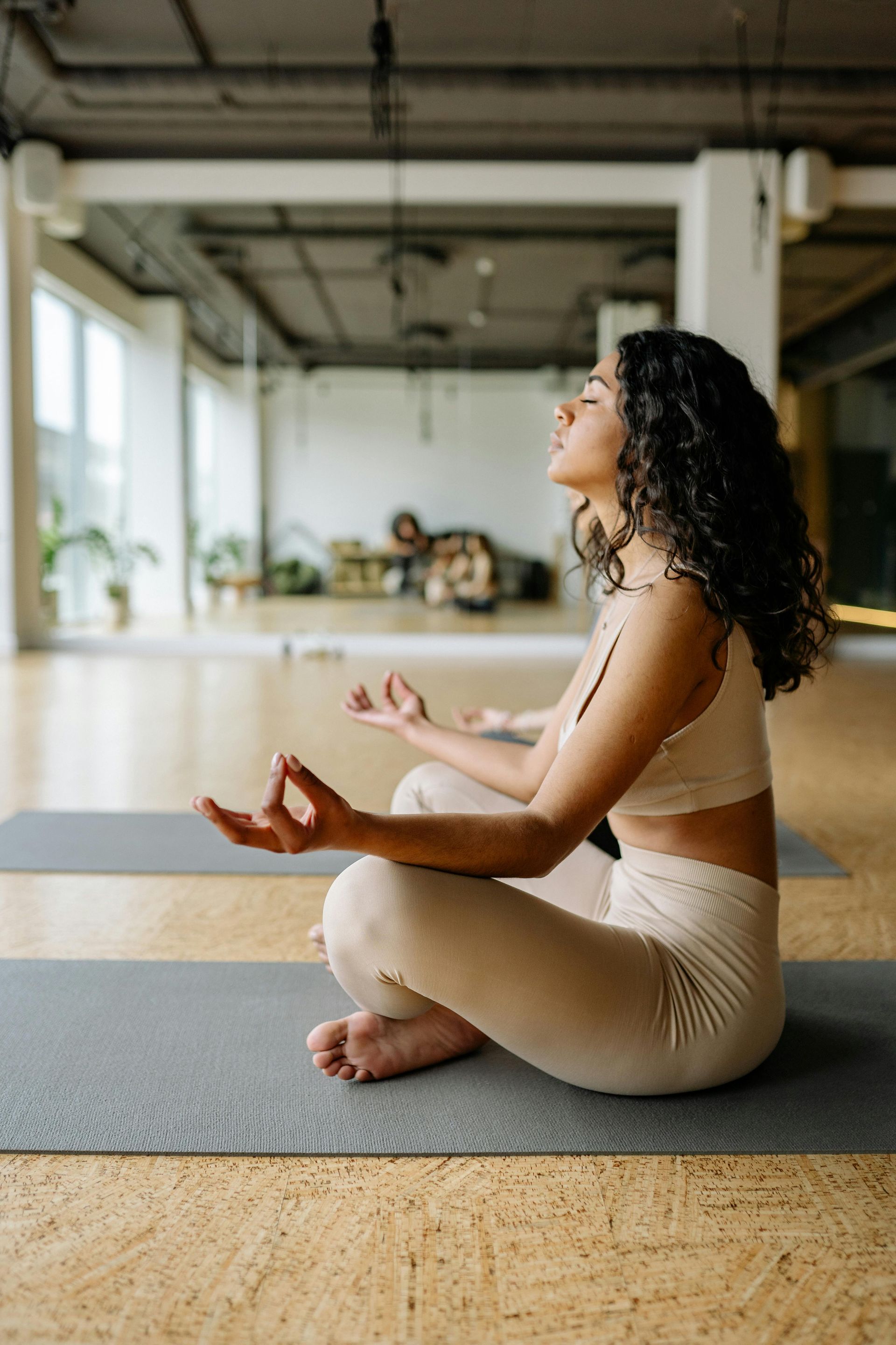 A woman is sitting on a yoga mat with her eyes closed in a yoga studio.
