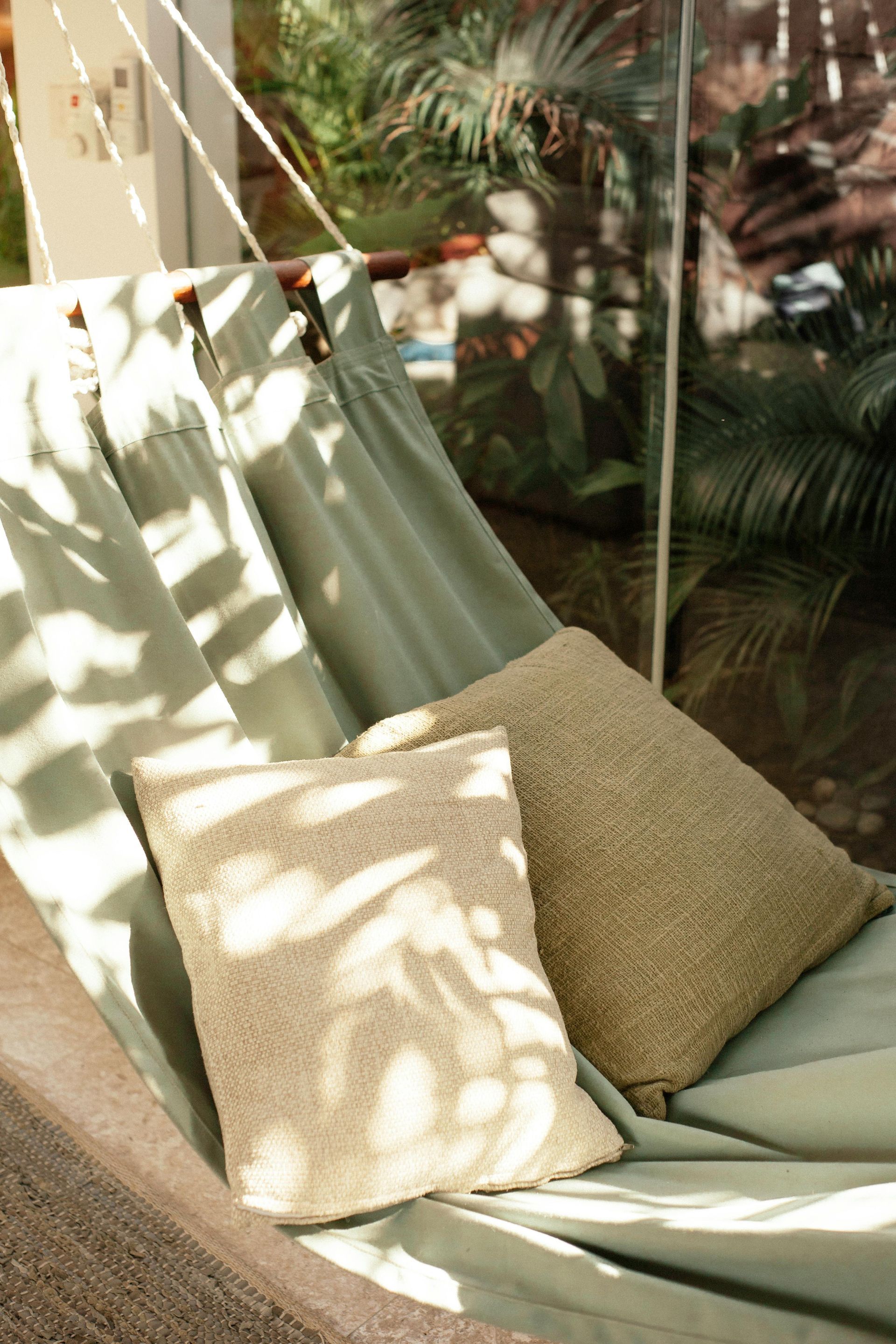 A hammock with two pillows on it in front of a window.