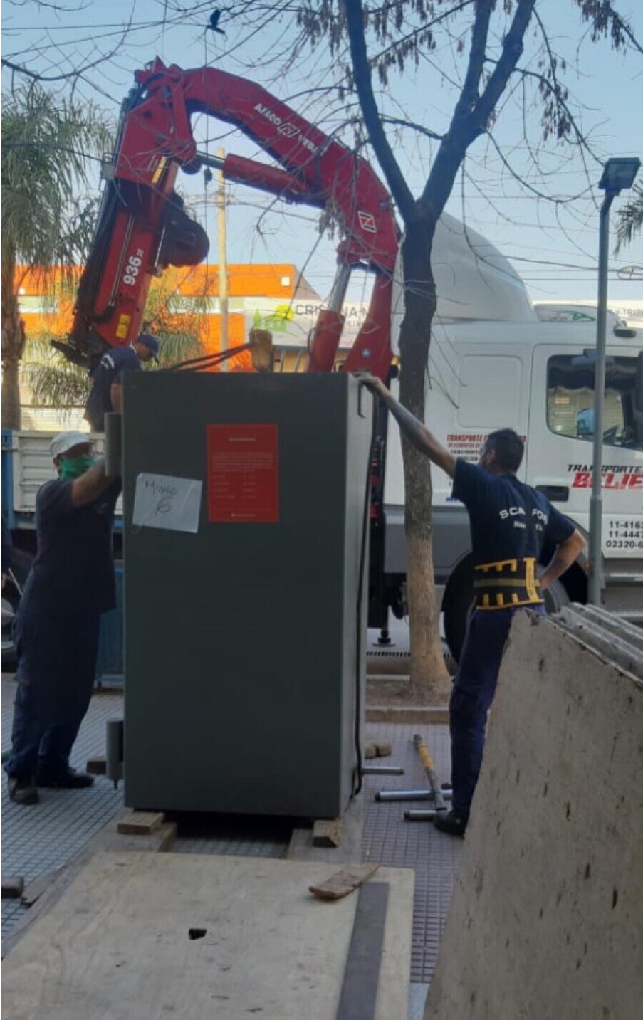 Se está utilizando una grúa para levantar una caja en una acera.