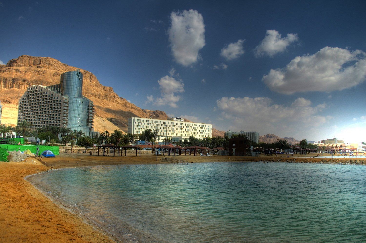 נוף חוף עם בניינים, הרים ומים כחולים תחת שמיים מעוננים חלקית.