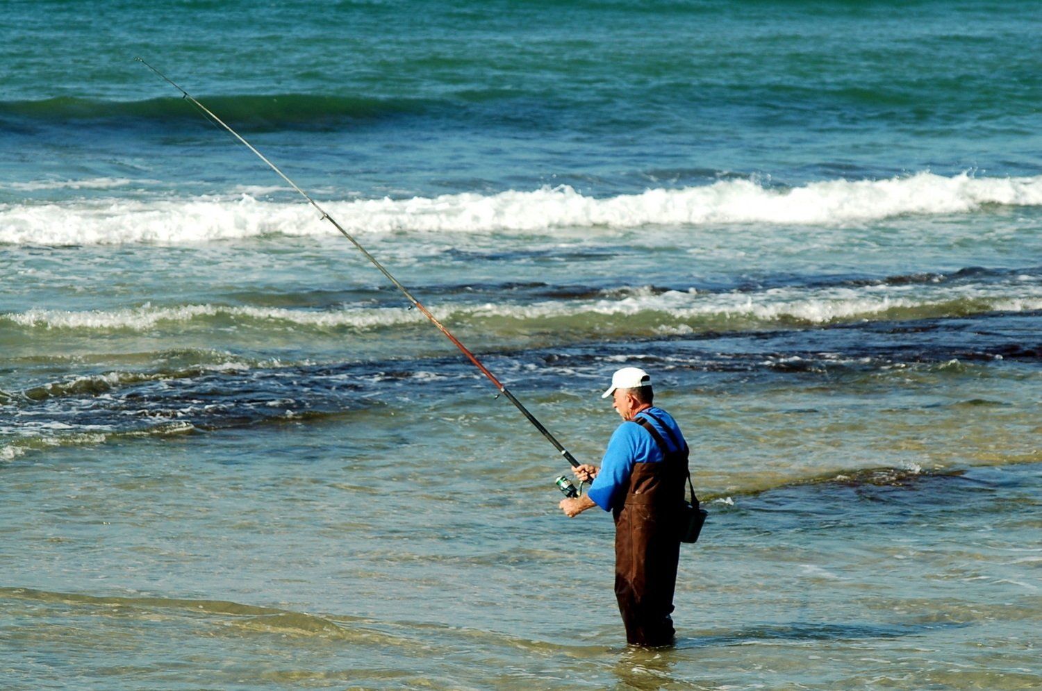 איש דג באוקיינוס, לובש מגפיים וכובע לבן. מים וגלים בצבע טורקיז.