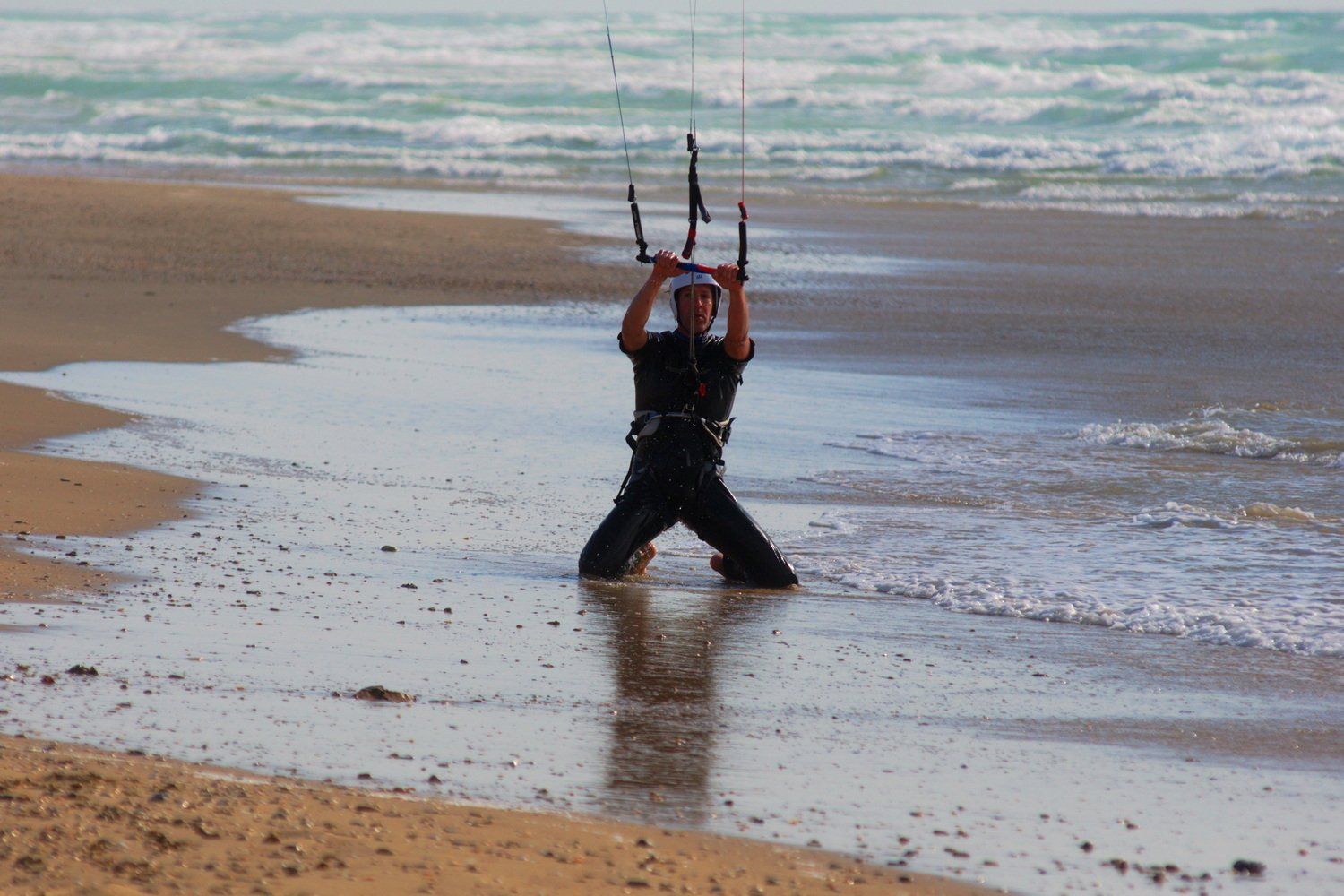 גבר כורע על חוף ים עם מוט שליטה לקייטבורד, גלים ברקע.