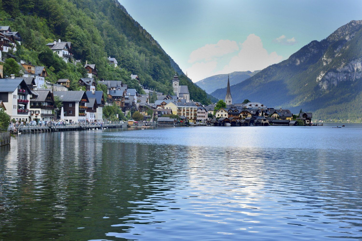 כפר שליו על שפת אגם, השוכן בין הרים ירוקים ושופעים, ובו צריח כנסייה.