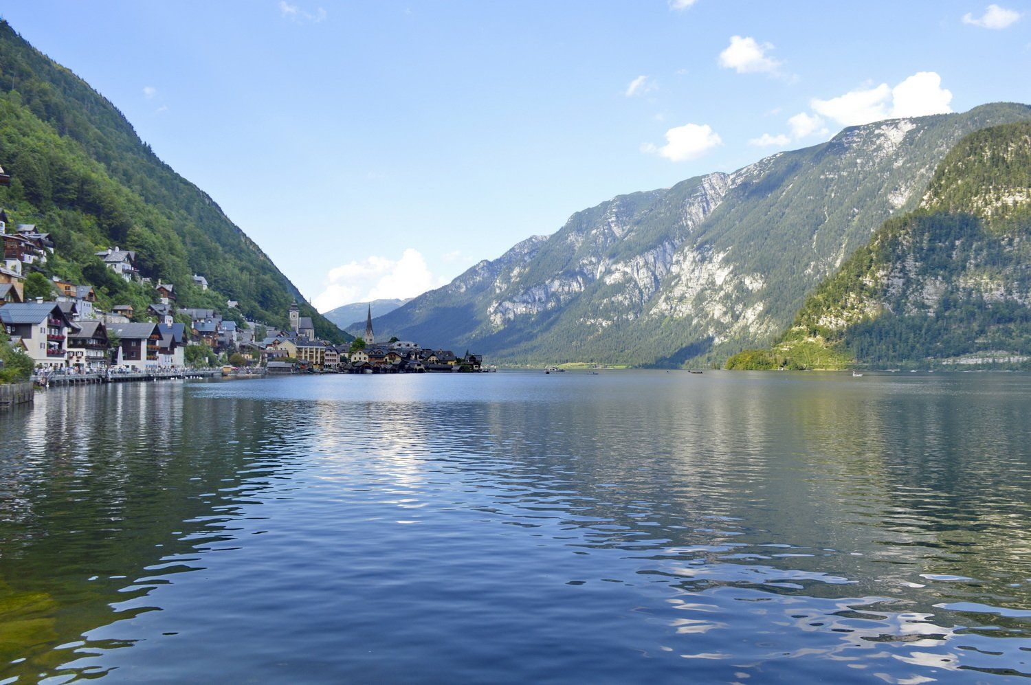 אגם האלשטאט, אוסטריה, עם כפר השוכן למרגלות הרים ירוקים תחת שמיים כחולים.