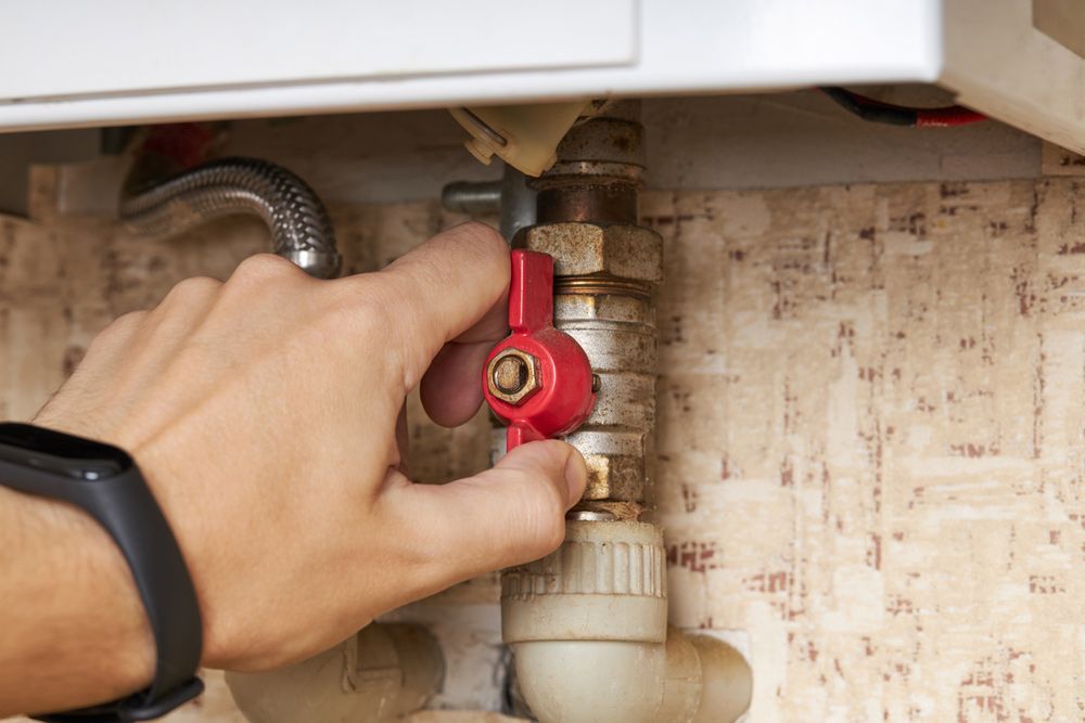 Person's Hand Turning a Red Valve on a Pipe Connected to a Boiler — B & A Plumbing & Gas In Wauchope, NSW