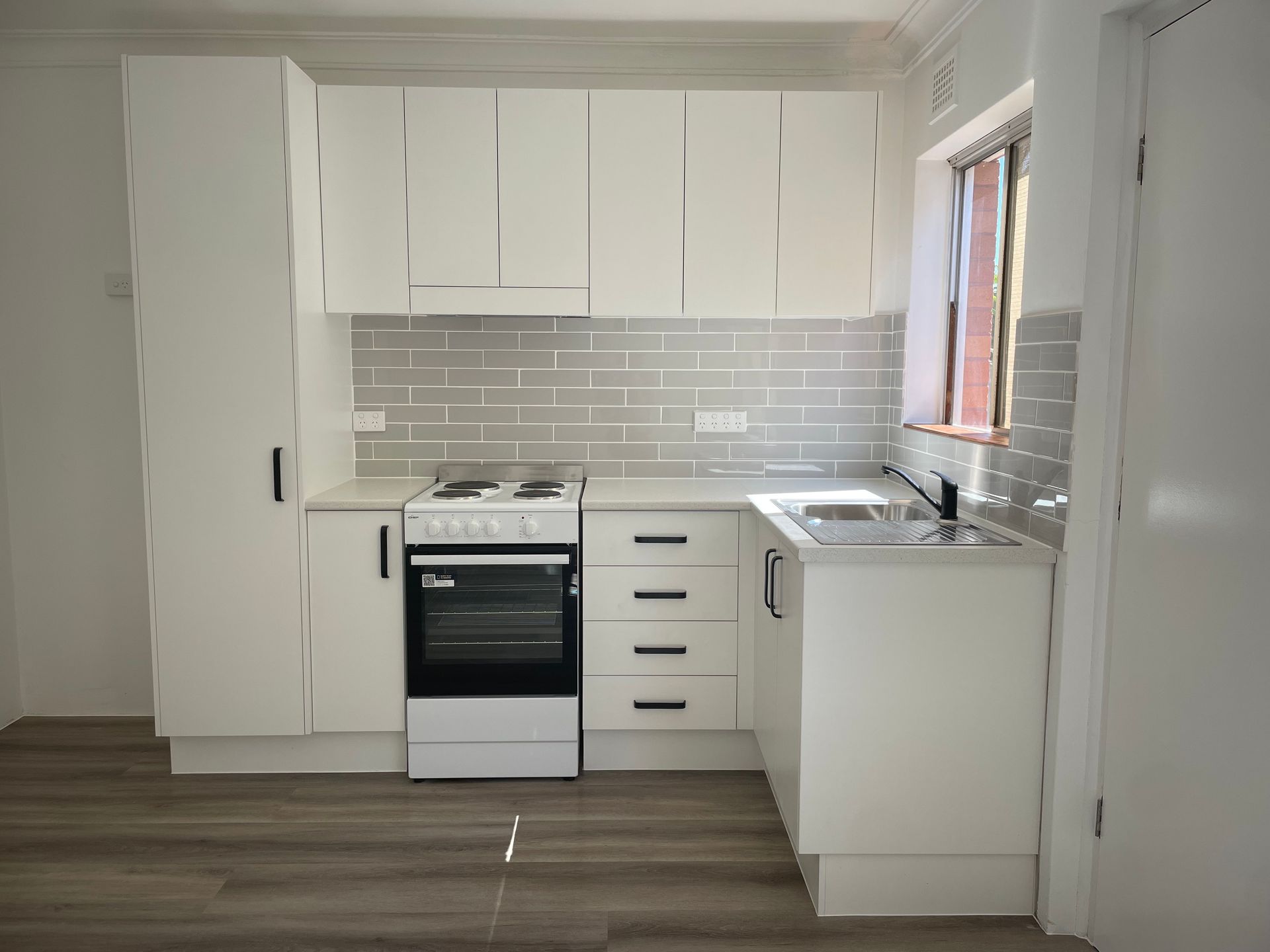 A modern white kitchen with wood-look flooring, subway tile backsplash, a stove, and a sink — B & A Plumbing & Gas In Wauchope, NSW