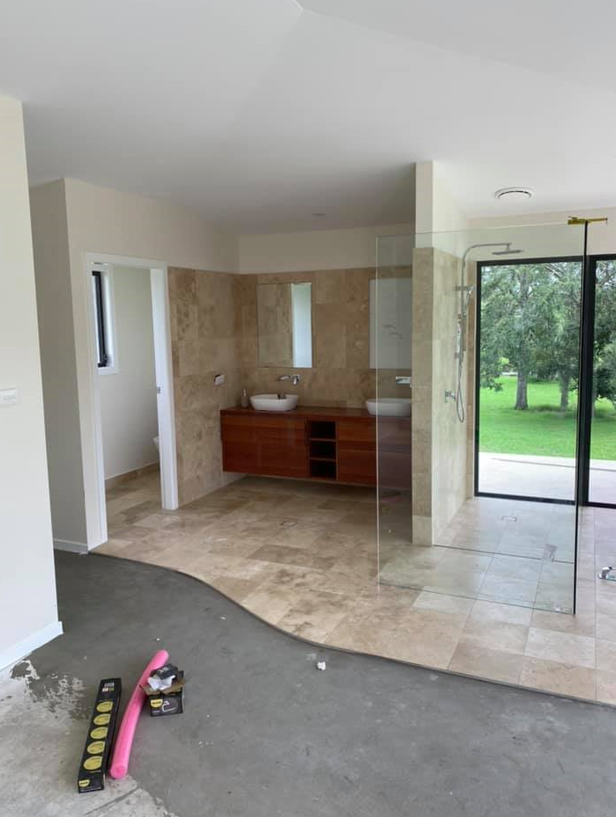 A bathroom under renovation featuring a vanity with two sinks, tile flooring, a glass shower, and concrete floor space  — B & A Plumbing & Gas In Wauchope, NSW