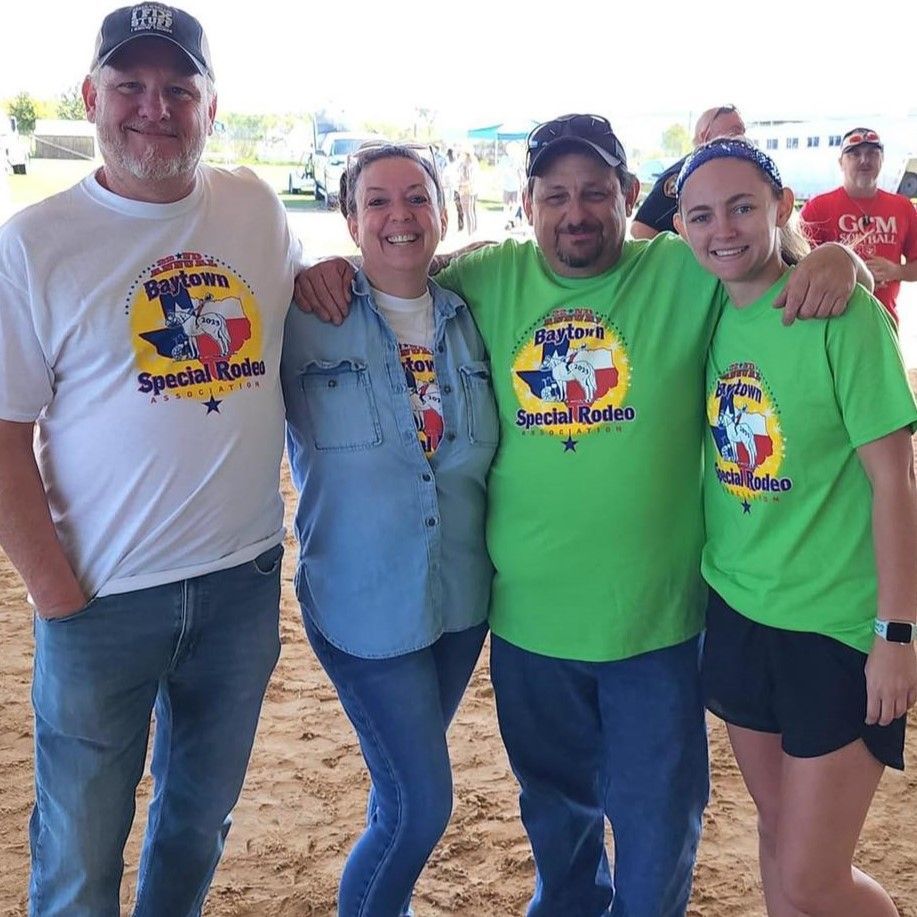 Four people smiling in Special Olympics T-shirts, standing together at an outdoor event.