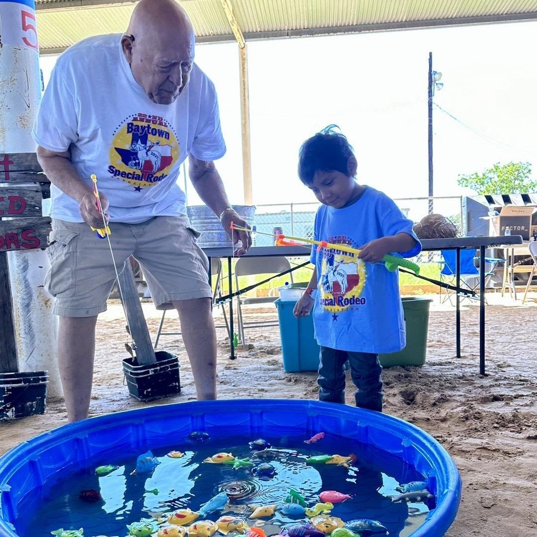 Two people fishing at a blue plastic pool filled with fish and water toys outdoors
